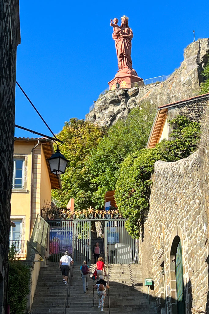 The statue Notre-Dame-de-France is a large bronze-colored statue that sits on another volcanic spike near the cathedral. The statue is of a woman holding a baby in her arms.